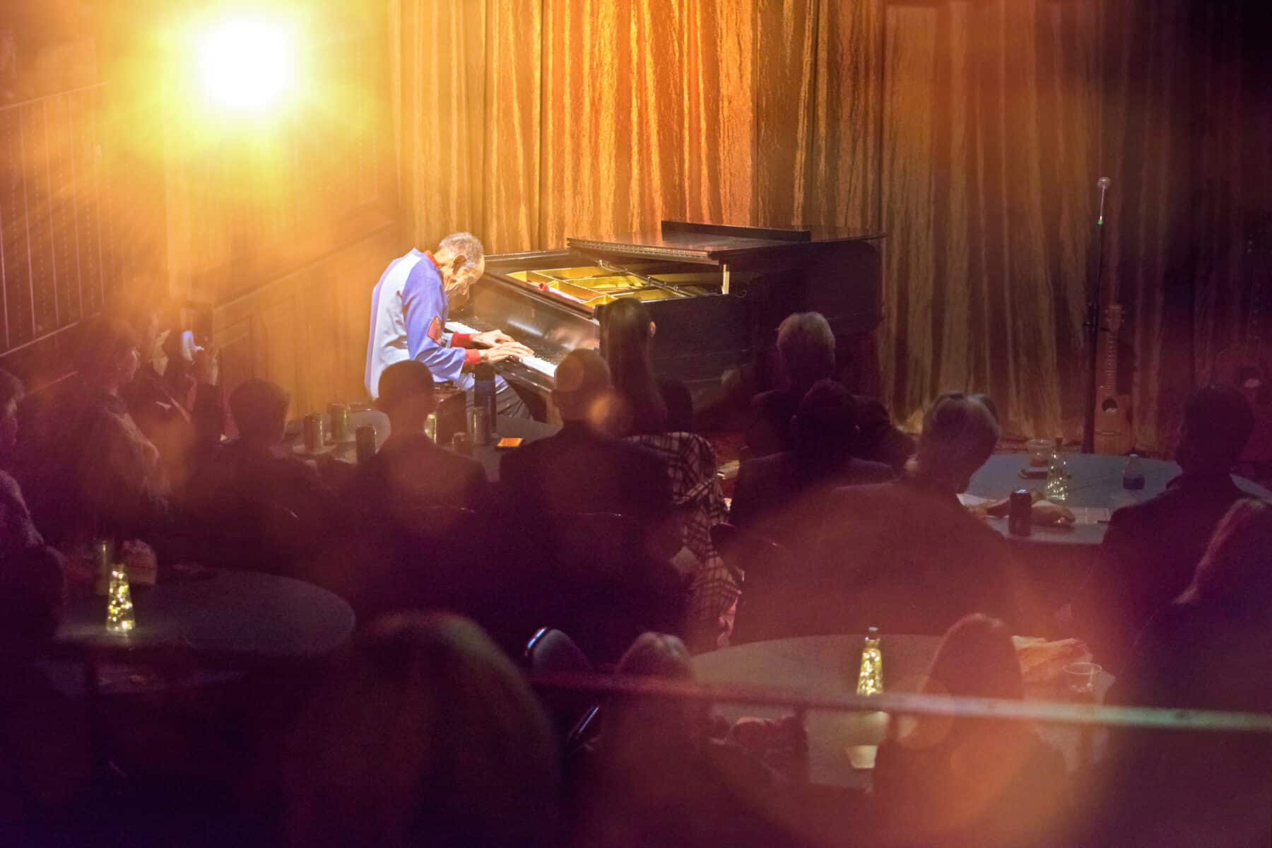 Charles Lewis performs at the ASU Kerr grand piano with flaring stage lights around him and a rapt audience
