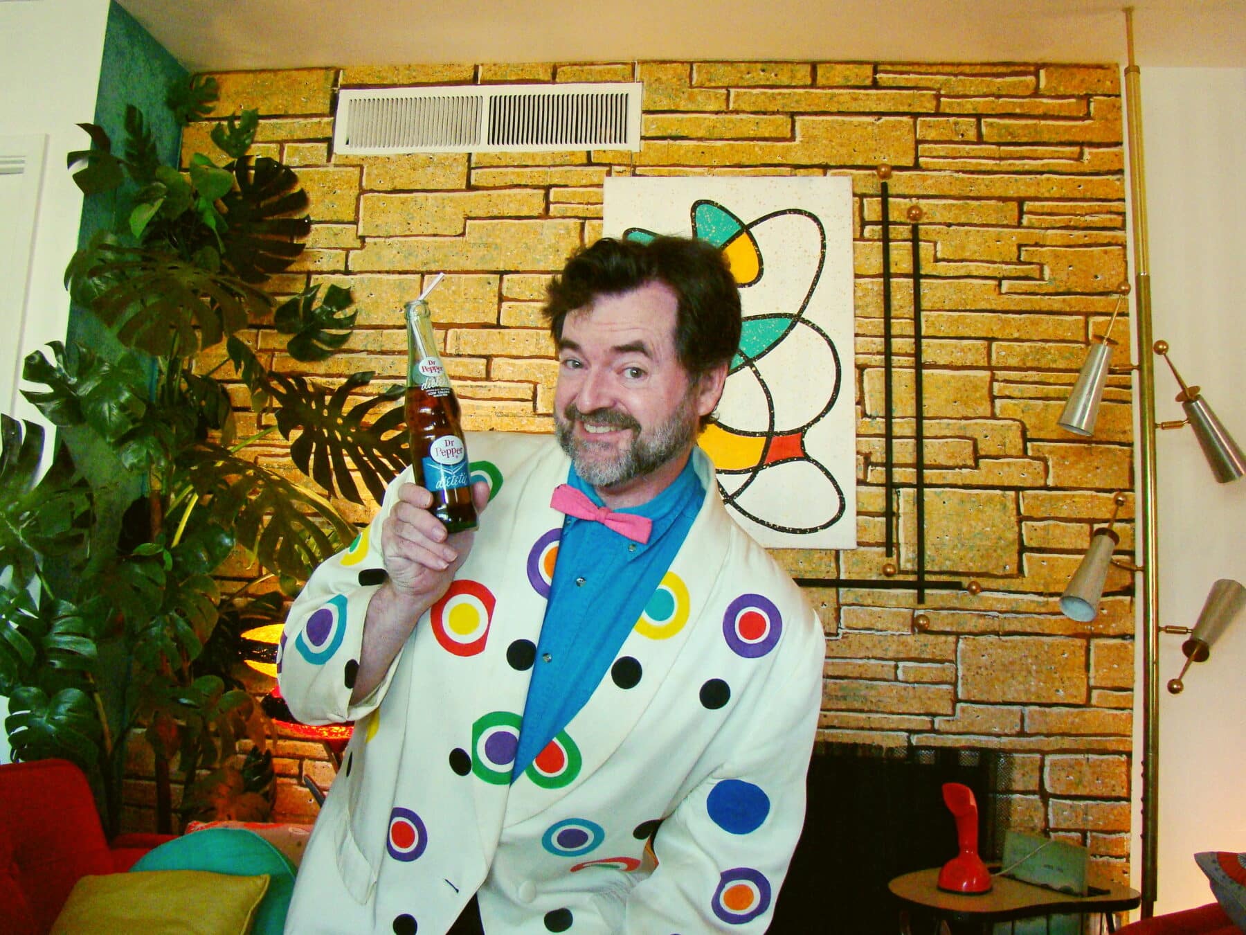 Paul Wilson poses with a glass bottle of soda in his bright and colorful 1950s styled home. 