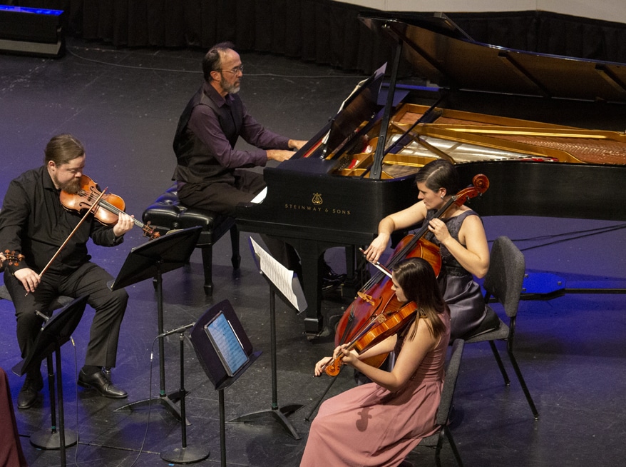 James D'León sits at the piano along with a violinist, violist, and cellist. 