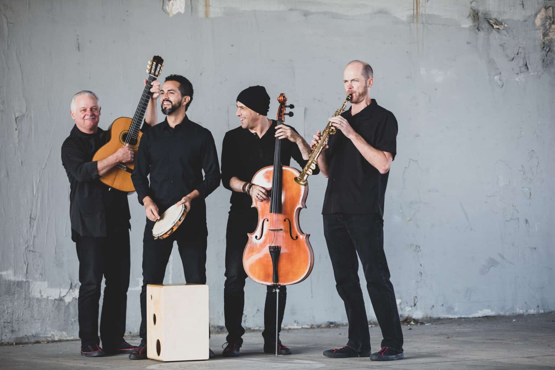 Quarteto Nuevo pose with their instruments against a concrete wall.