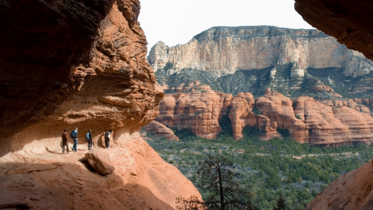 Hikers step along the edge of red rock formations