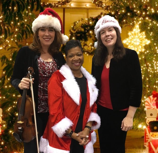 We3 poses in front of holiday lights and decor with Suzanne Lansford and Nicole Pesce in Santa hats and Renee Patrick in a stylish red Santa jacket