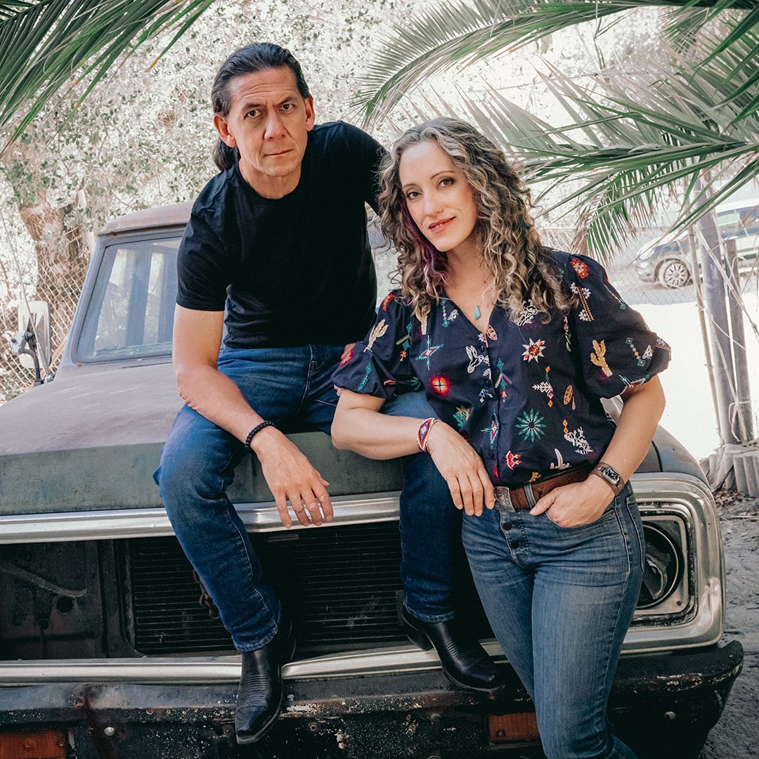 Joselyn and Don lean against a classic American car under palm trees