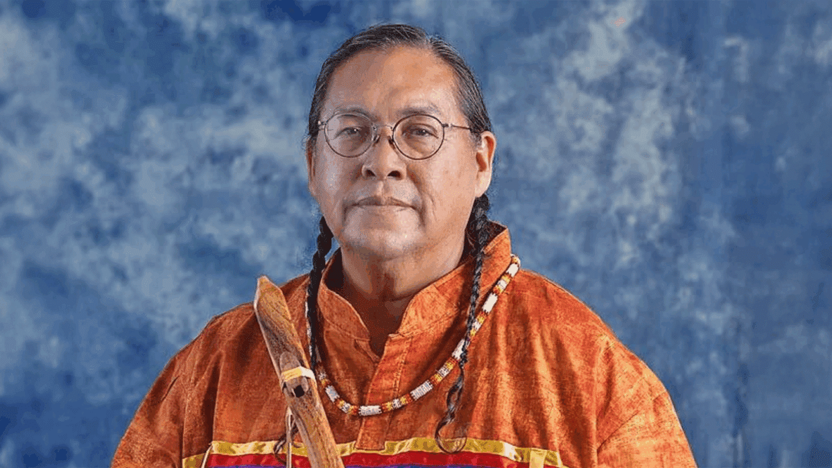 Aaron White poses in an orange shirt with a handcrafted Native American Flute