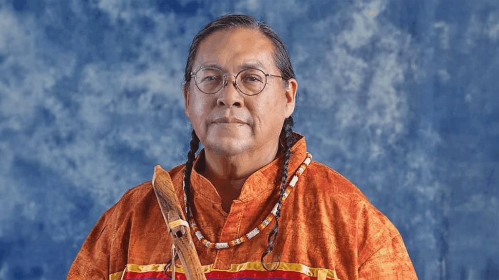 Aaron White poses in an orange shirt with a handcrafted Native American Flute