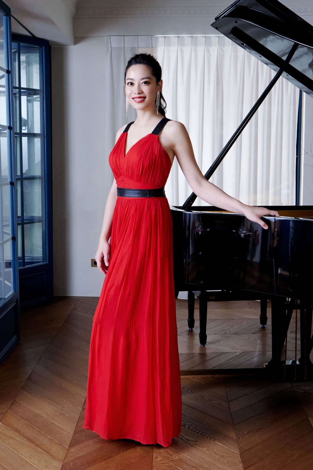 A woman in a red dress stands beside a piano, showcasing elegance and musicality in a stylish setting.