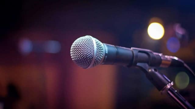 Close up photo of a microphone in a dark room with a stage light behind it.
