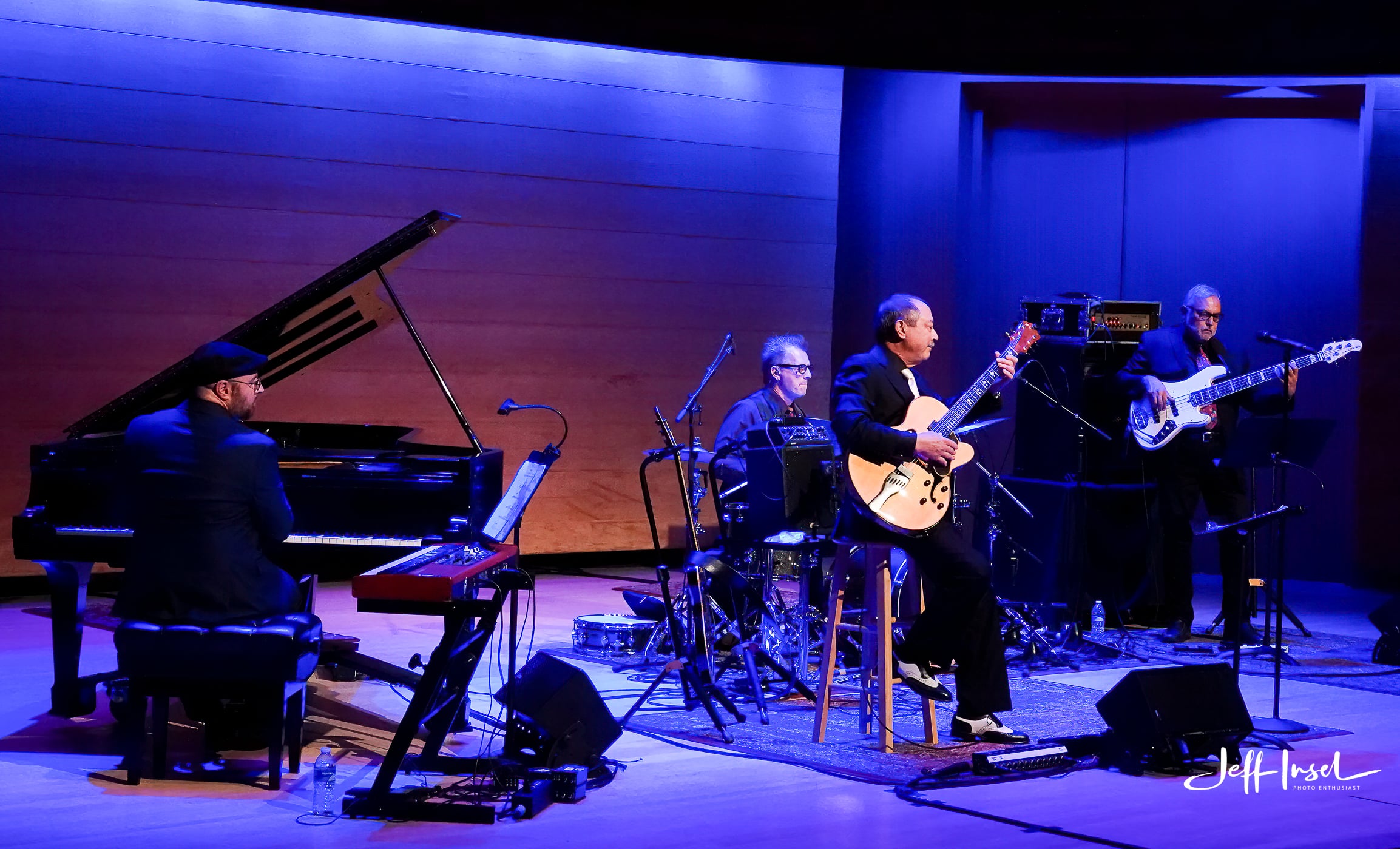 A band performing on stage, featuring a pianist and a guitarist, with vibrant lighting.