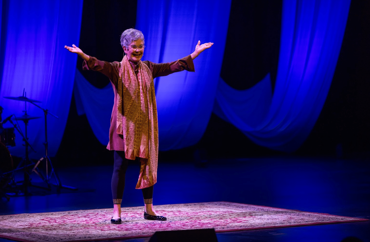 Dr. Jane Vogel Mantiri stands onstage whilst performing See Jane Run, arms outstretched